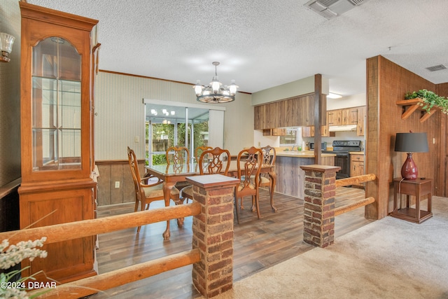 dining room featuring wood walls, wood-type flooring, a textured ceiling, and a notable chandelier