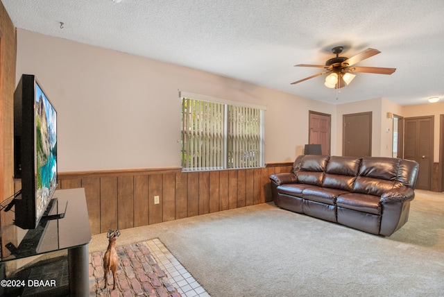 living room featuring carpet flooring, wooden walls, ceiling fan, and a textured ceiling