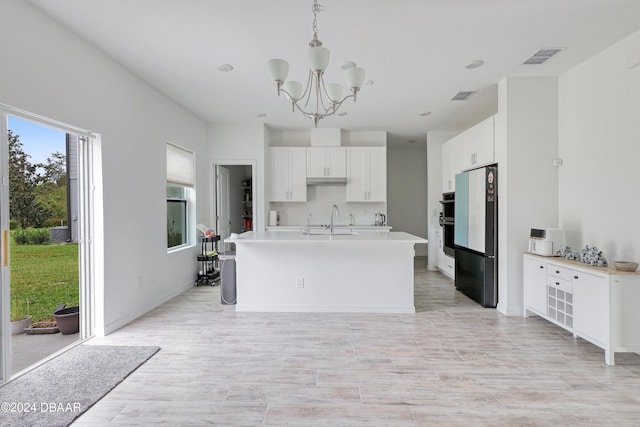 kitchen featuring white cabinetry, a notable chandelier, black refrigerator, hanging light fixtures, and sink