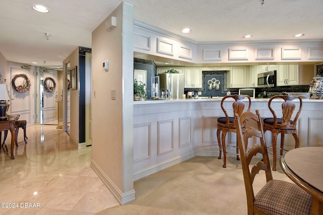 kitchen featuring kitchen peninsula, appliances with stainless steel finishes, a kitchen bar, a textured ceiling, and light colored carpet