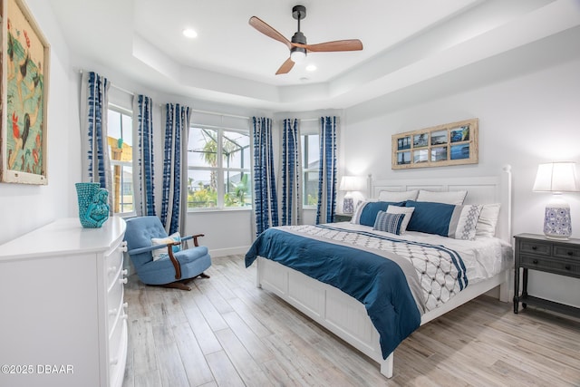 bedroom featuring ceiling fan, light hardwood / wood-style floors, and a raised ceiling