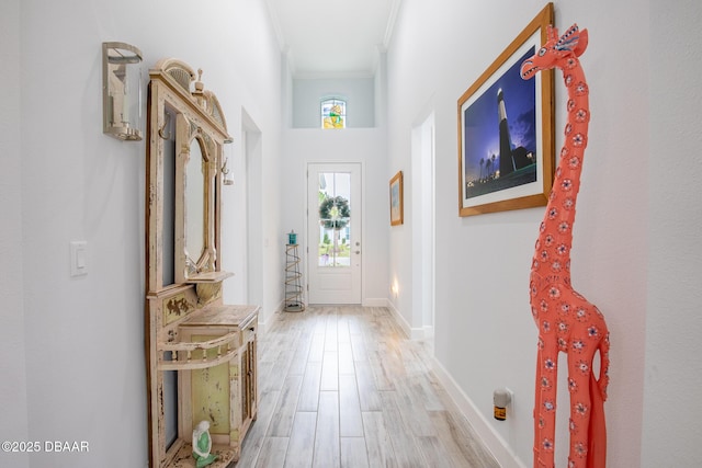 doorway to outside with light wood-type flooring, ornamental molding, and a towering ceiling