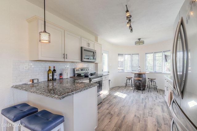 kitchen featuring a breakfast bar, light hardwood / wood-style flooring, dark stone countertops, appliances with stainless steel finishes, and decorative light fixtures