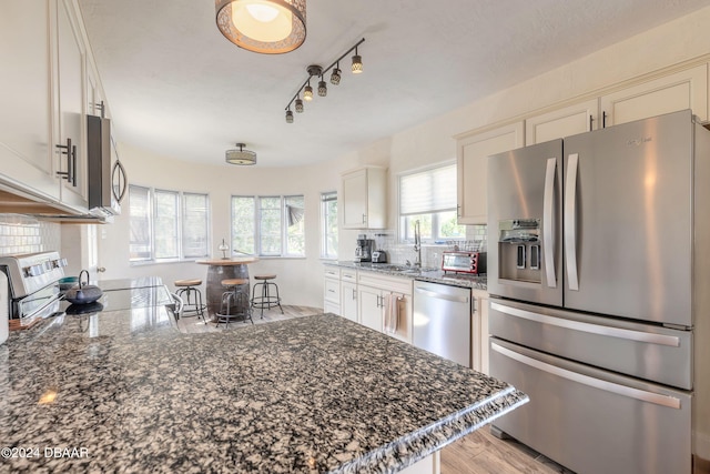 kitchen with decorative backsplash, dark stone counters, stainless steel appliances, sink, and light hardwood / wood-style floors