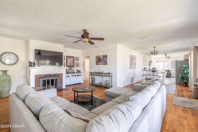 living room featuring a brick fireplace, ceiling fan, and light hardwood / wood-style flooring