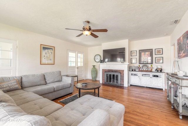 living room with ceiling fan, wood-type flooring, a textured ceiling, and a brick fireplace