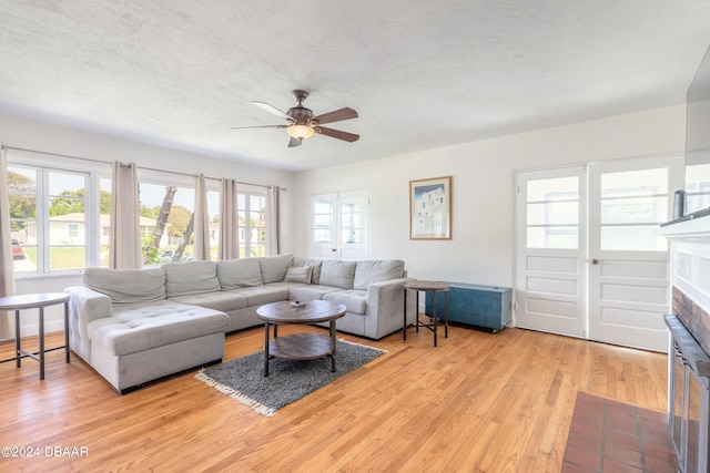 living room with a fireplace, a textured ceiling, light hardwood / wood-style floors, and ceiling fan