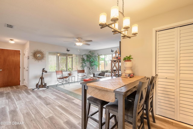 dining area with ceiling fan with notable chandelier and light hardwood / wood-style floors