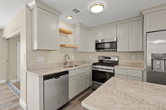 kitchen with appliances with stainless steel finishes, sink, a textured ceiling, and light hardwood / wood-style flooring