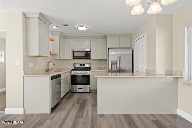 kitchen with sink, light wood-type flooring, kitchen peninsula, and appliances with stainless steel finishes