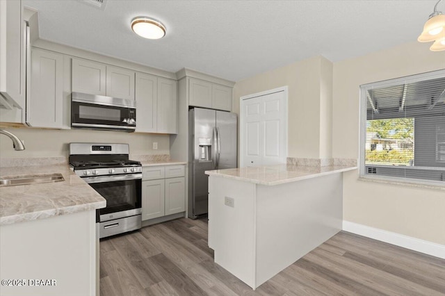 kitchen with sink, stainless steel appliances, decorative light fixtures, kitchen peninsula, and light wood-type flooring