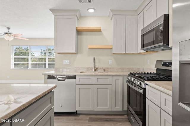 kitchen featuring sink, light wood-type flooring, appliances with stainless steel finishes, ceiling fan, and light stone countertops