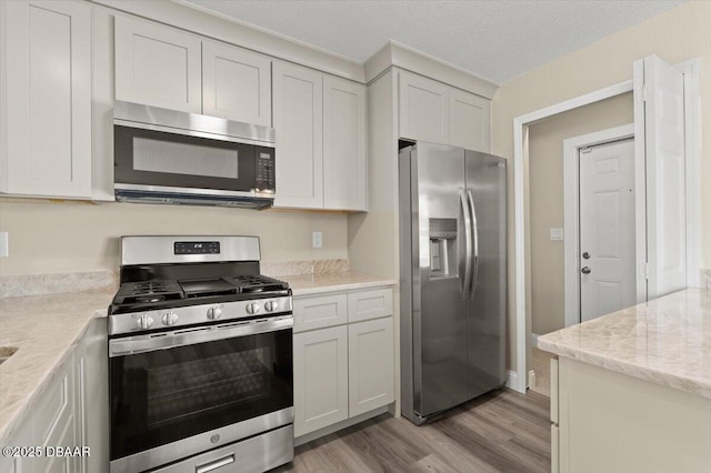 kitchen with light stone countertops, stainless steel appliances, light hardwood / wood-style floors, and white cabinets