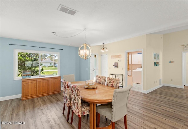 dining room featuring washer / dryer, light hardwood / wood-style flooring, and an inviting chandelier