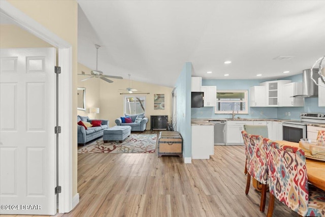 interior space with stainless steel appliances, vaulted ceiling, wall chimney range hood, light hardwood / wood-style flooring, and white cabinetry