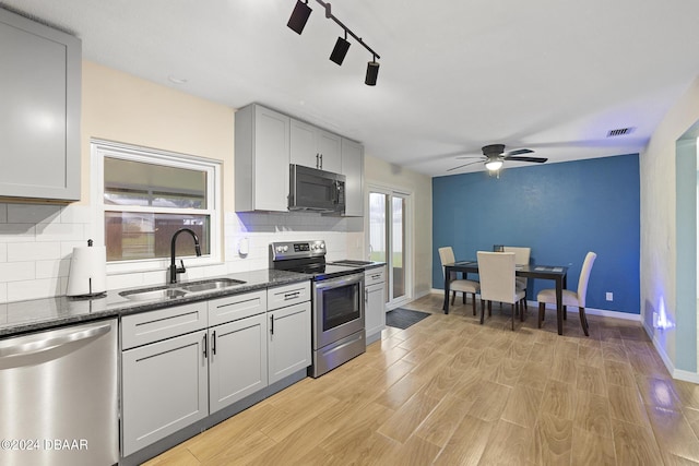 kitchen with sink, dark stone counters, gray cabinets, stainless steel appliances, and light hardwood / wood-style floors