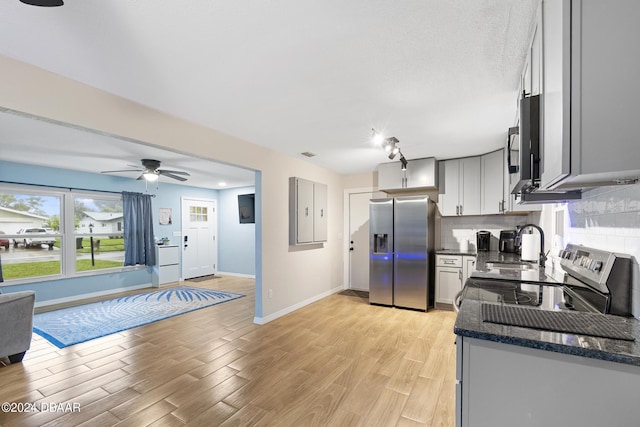 kitchen featuring sink, light hardwood / wood-style flooring, appliances with stainless steel finishes, tasteful backsplash, and dark stone counters