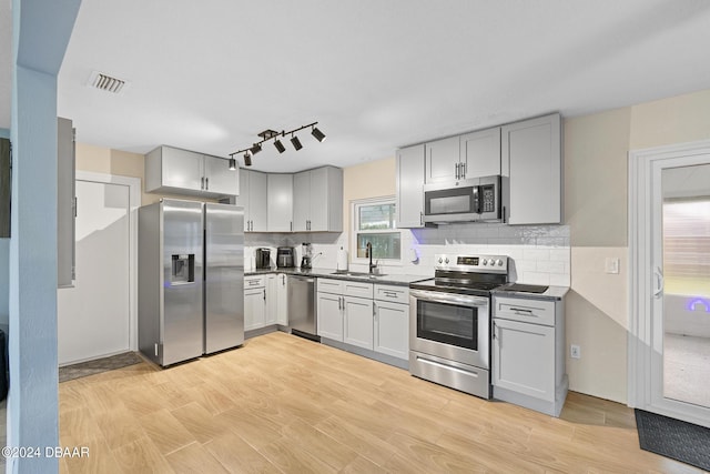 kitchen with sink, light hardwood / wood-style flooring, gray cabinets, appliances with stainless steel finishes, and tasteful backsplash