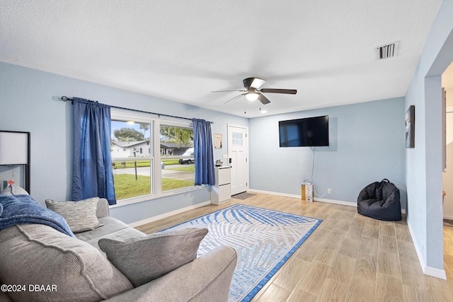 living room with ceiling fan, a textured ceiling, and light wood-type flooring