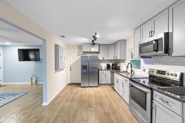 kitchen with sink, appliances with stainless steel finishes, tasteful backsplash, light hardwood / wood-style floors, and dark stone counters