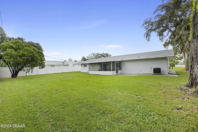 back of property with central AC unit, a sunroom, and a lawn