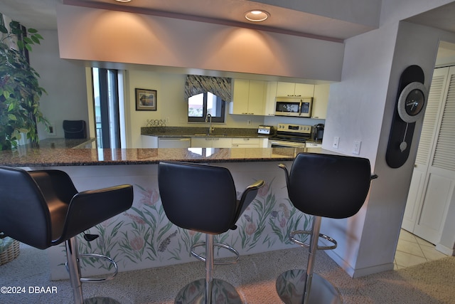 kitchen featuring dark stone counters, appliances with stainless steel finishes, sink, a breakfast bar, and kitchen peninsula