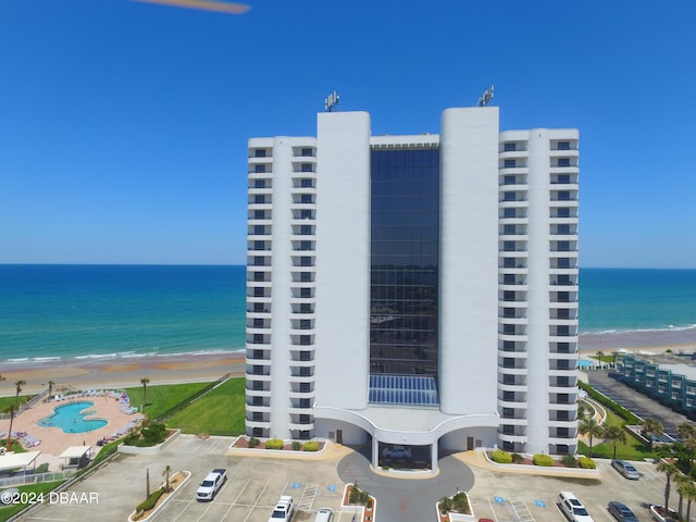 view of building exterior featuring a view of the beach, a water view, and a community pool