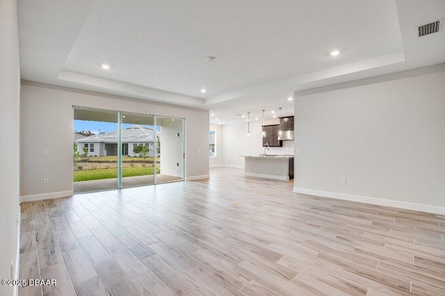 unfurnished living room featuring sink, light hardwood / wood-style floors, and a raised ceiling