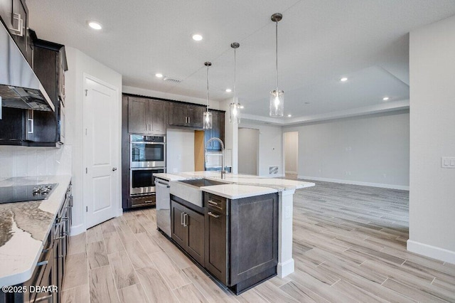 kitchen featuring an island with sink, appliances with stainless steel finishes, sink, and light stone counters