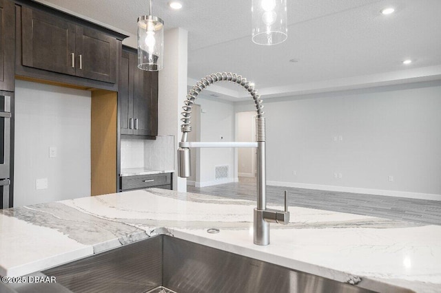 kitchen featuring dark brown cabinetry, sink, light stone counters, decorative light fixtures, and oven