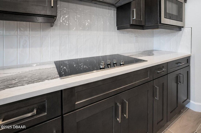 kitchen featuring light stone counters, wood-type flooring, black electric cooktop, stainless steel microwave, and decorative backsplash