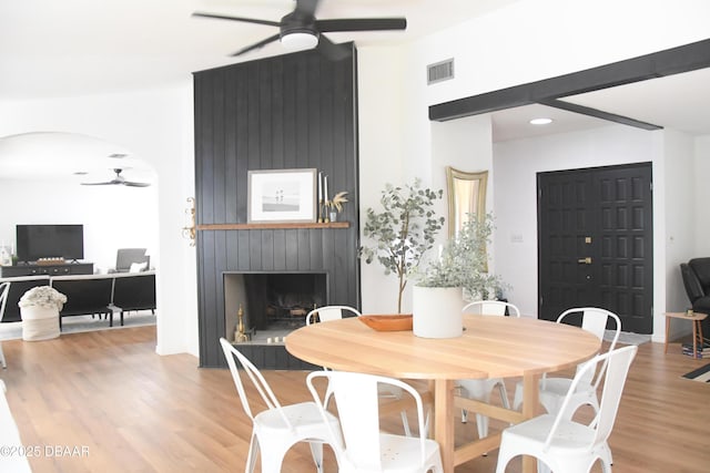 dining space featuring ceiling fan, wood finished floors, a large fireplace, and arched walkways