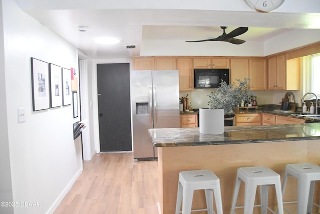 kitchen with stainless steel fridge with ice dispenser, black microwave, light wood-type flooring, a sink, and a breakfast bar
