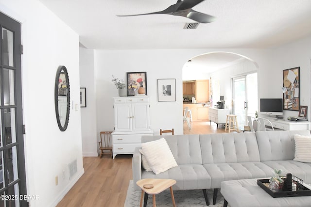 living area featuring arched walkways, a ceiling fan, light wood-type flooring, and baseboards