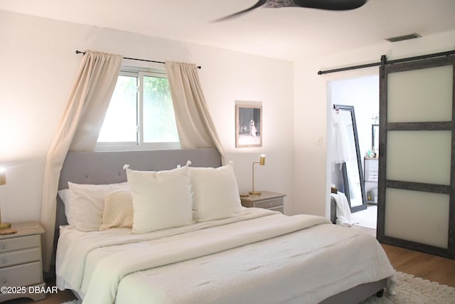 bedroom with wood finished floors, a ceiling fan, and a barn door