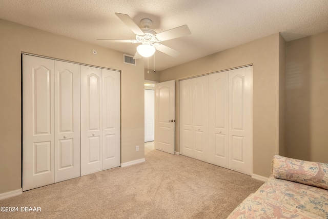 unfurnished bedroom featuring light carpet, a textured ceiling, two closets, and ceiling fan