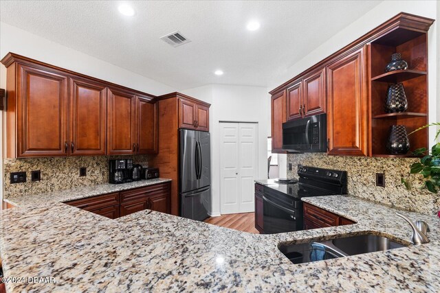 kitchen with decorative backsplash, light wood-type flooring, light stone countertops, and black appliances