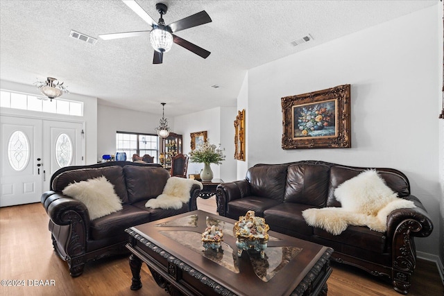 living room featuring ceiling fan with notable chandelier, a textured ceiling, and light hardwood / wood-style flooring