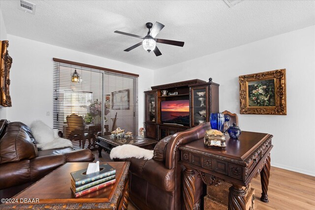 living room featuring ceiling fan, light hardwood / wood-style floors, and a textured ceiling