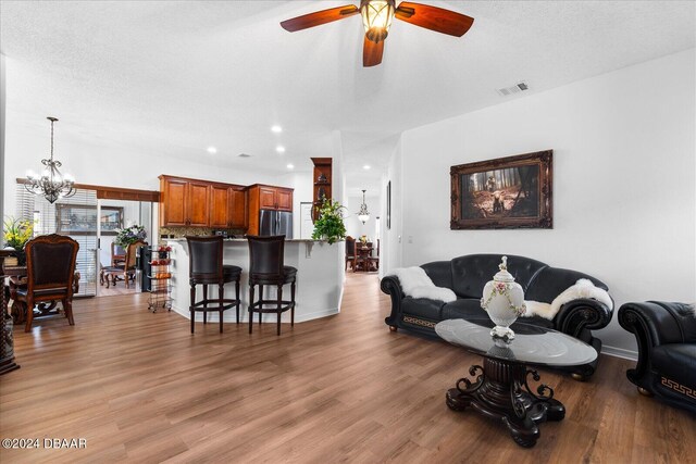 living room featuring a textured ceiling, wood-type flooring, and ceiling fan with notable chandelier