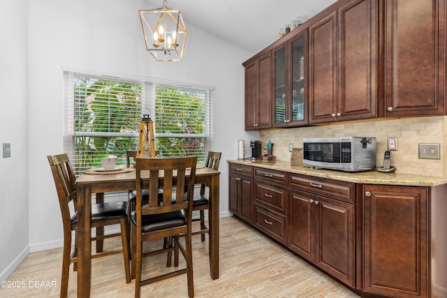 kitchen with light hardwood / wood-style flooring, backsplash, light stone counters, decorative light fixtures, and vaulted ceiling