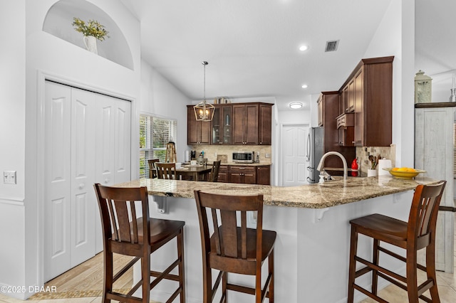 kitchen featuring tasteful backsplash, hanging light fixtures, light stone counters, and vaulted ceiling