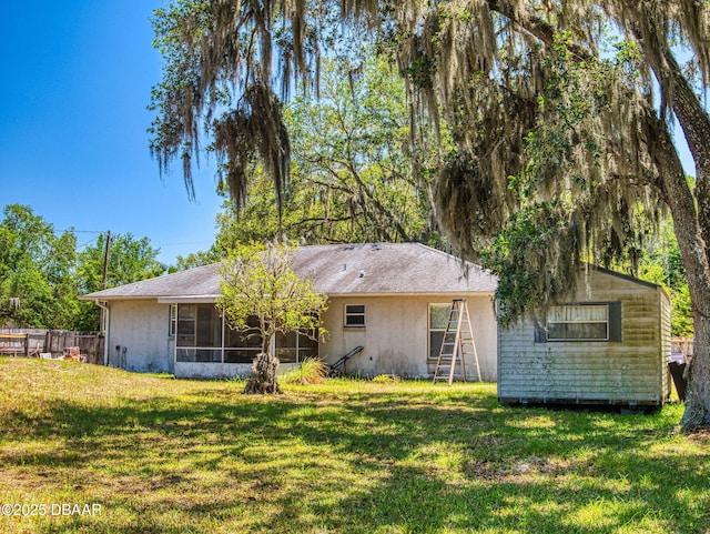 back of house with a yard, an outbuilding, fence, stucco siding, and a sunroom