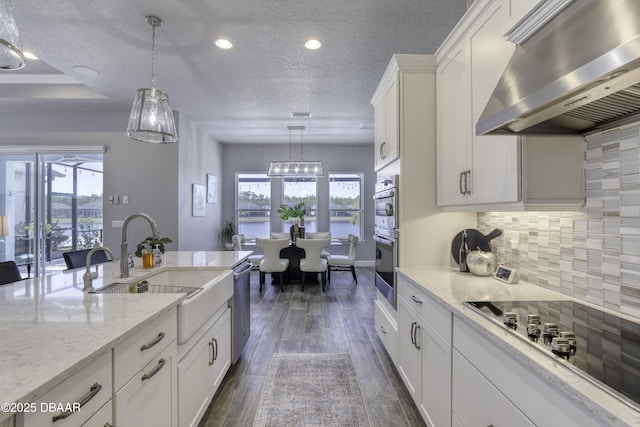 kitchen featuring decorative light fixtures, ventilation hood, sink, white cabinets, and black cooktop