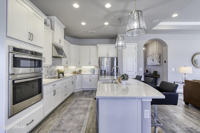 kitchen with sink, white cabinetry, a center island with sink, stainless steel appliances, and a kitchen bar