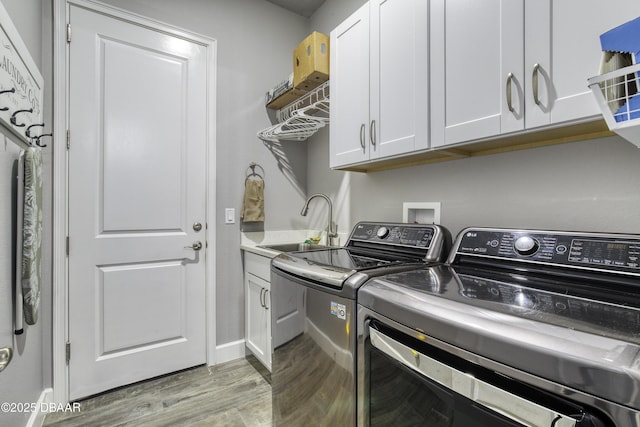 clothes washing area with cabinets, sink, independent washer and dryer, and light hardwood / wood-style floors