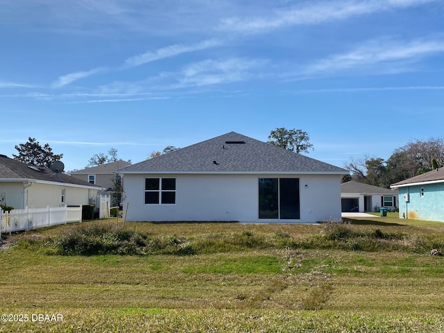 rear view of house featuring a shingled roof, fence, a lawn, and stucco siding