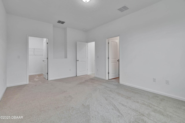 unfurnished bedroom with carpet, visible vents, a walk in closet, and baseboards