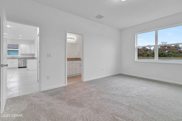 unfurnished bedroom featuring baseboards, visible vents, light colored carpet, ensuite bath, and a sink