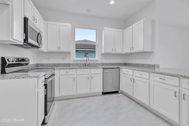 kitchen with stainless steel appliances, a sink, white cabinetry, and light stone countertops